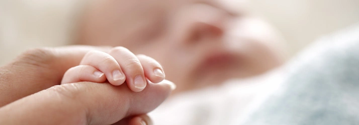 lose-up of a baby gently holding an adult’s finger