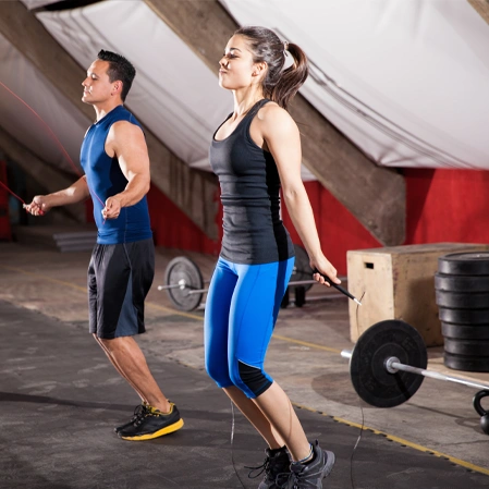 Two people exercising in a gym, jumping rope